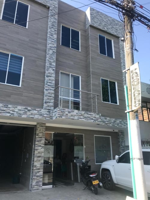 Fachada del Hotel Maderos Cali con diseño moderno de ladrillo gris, amplios ventanales y entrada a nivel de calle con vehículo blanco estacionado