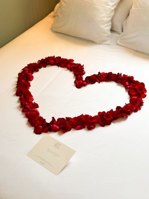 Pétalos de rosa roja arreglados en forma de corazón en una cama blanca del Hotel La Prison, Béziers