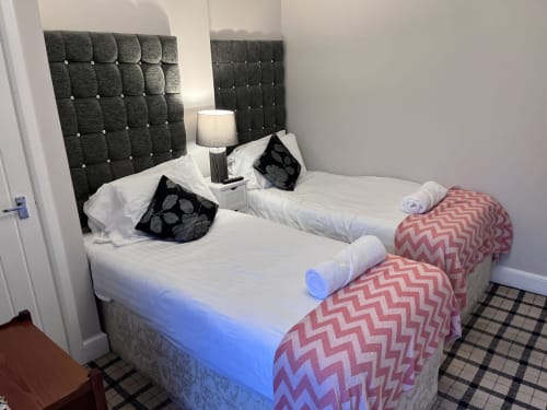 Twin beds with dark tufted headboards, white linens, rolled towels, and decorative pillows in The Railway Hotel's Shaftoe