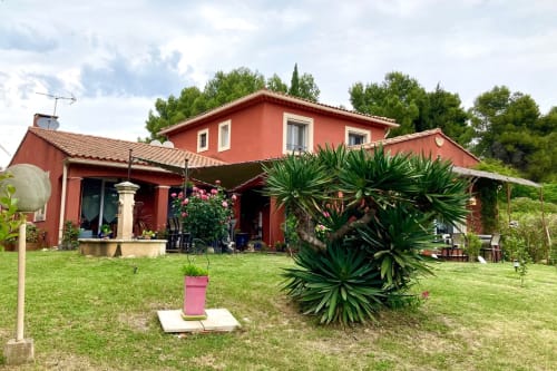 Red cottage at Domaine des Lavarines in Morières-lès-Avignon with green lawn, tropical plants, and covered patio area