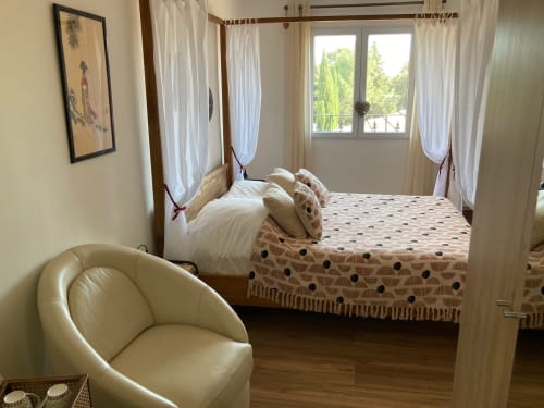 Spacious bedroom at Domaine des Lavarines cottage with four-poster bed, cream armchair, and garden view windows with sheer