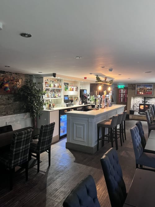 Modern bar lounge at The Railway Hotel Haydon Bridge with grey island counter, plaid seating, and ambient lighting