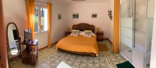 Bright bedroom with orange bedding at Domaine des Lavarines cottage, featuring patterned tile floor, wooden furniture, and