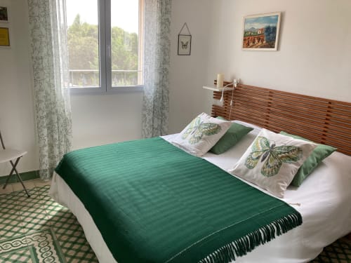 Bright cottage bedroom with green blanket, butterfly pillows, wooden headboard, garden views through large windows at Domaine