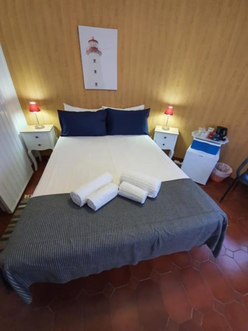 Habitación doble económica en el albergue Ocean View Lagos con almohadas azul marino, toallas blancas, lámparas de mesita y arte de faro