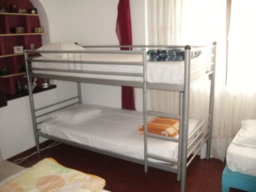 Metal bunk bed with white bedding in a dorm room at Ocean View Lagos hostel in Lagos, featuring shelving and garden view