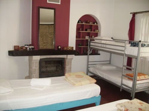 Hostel dorm room at Ocean View Lagos with single bed, metal bunk bed, fireplace, arched shelving, and garden view windows in