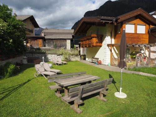 Alpine garden with wooden picnic table, lounge chairs, and mountain views at Residence Rodolon, Mazzin