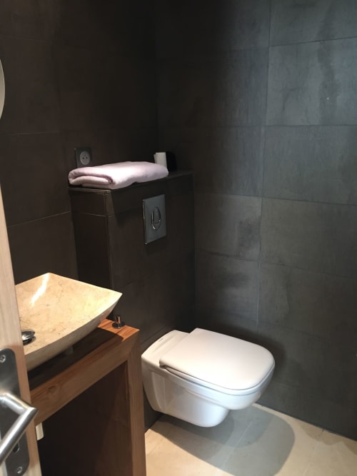 Modern bathroom in The Perch apartment at AJOUCADOU, Lourmarin with white toilet, marble sink, and dark tile walls