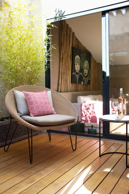 Cozy outdoor terrace at AJOUCADOU Lourmarin with wicker chair, pink cushions, and modern bedroom view through glass doors