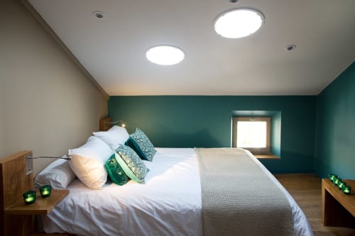 Modern bedroom at AJOUCADOU Lourmarin with teal accent wall, white bedding, wooden furniture, and recessed lighting
