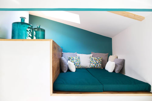Cozy turquoise reading nook at AJOUCADOU Lourmarin with cushioned seating, colorful pillows, and wooden headboard