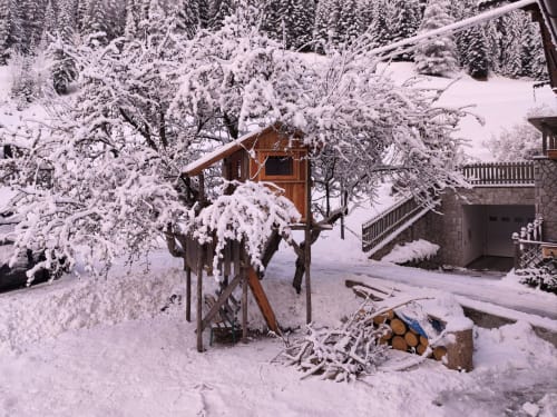 Schneebedeckter Baumhaus-Spielplatz in der Residenza Rodolon in Mazzin, umgeben von Wald und Bergen