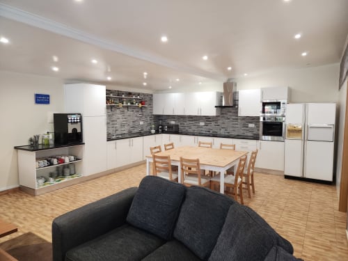 Modern open-plan kitchen and dining area at Ocean View Lagos hostel with white cabinetry, wooden table, and comfortable