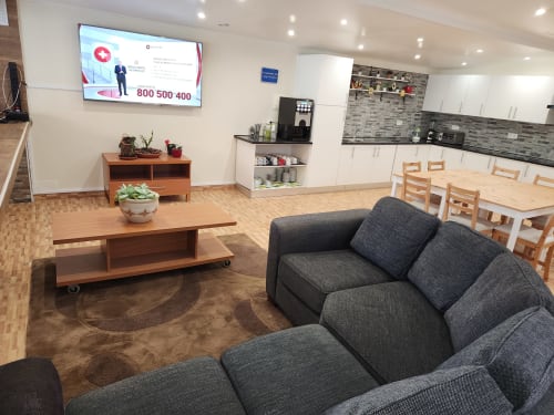 Ocean View Lagos hostel common area with gray sofas, wooden table, kitchen, dining area, and flat-screen TV