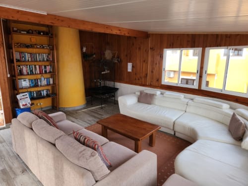 Spacious common lounge at Ocean View Lagos hostel with beige sofas, wooden furniture, bookshelf, and yellow column.