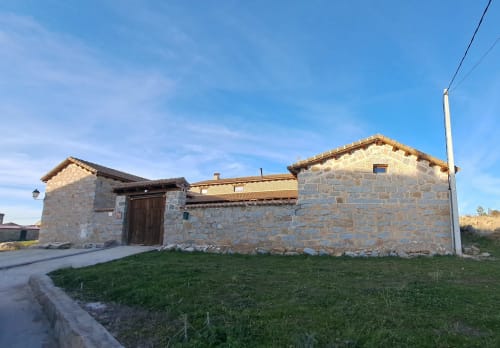 Exterior de casa de piedra en Apartamentos Turísticos Ávila con vistas a la montaña, jardines verdes y arquitectura tradicional