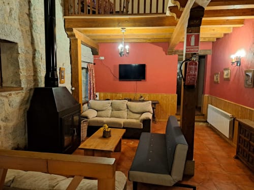 Acogedora sala de estar rústica en Ávila con chimenea, sofá beige, televisor, vigas de madera y paredes rojas