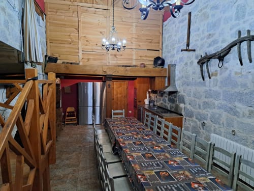 Comedor rústico en Ávila con vigas de madera, muros de piedra, mesa larga y cocina moderna