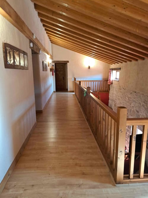 Amplio pasillo de nivel superior con vigas de madera y barandilla en casita Apartamentos Turísticos Ávila, piso de madera en toda su extensión
