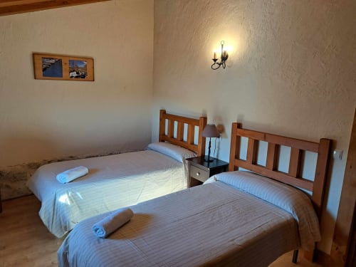 Dormitorio doble en Apartamentos Turísticos Ávila con camas de madera, vistas a la montaña, aplique de pared y luz natural