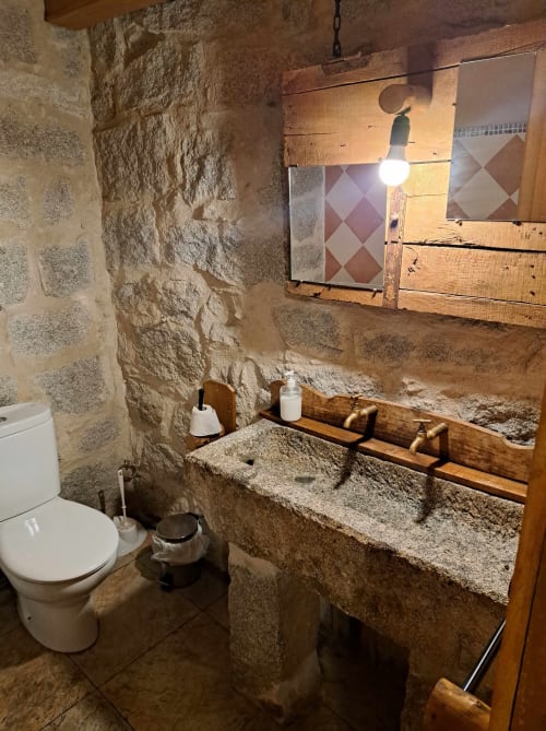 Baño rústico de piedra en Apartamentos Turísticos Ávila con lavabo natural, detalles de madera y espejo