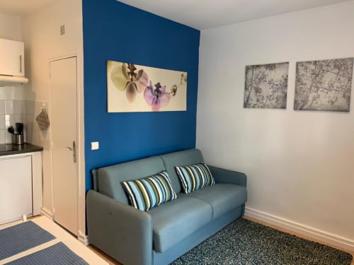 Gray sofa bed with striped pillows in Azur Studios Cannes Superior Studio, blue accent wall, kitchenette visible