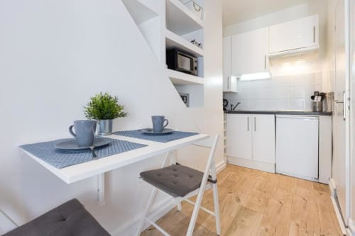 Compact kitchenette with dining table at Azur Studios Cannes, featuring white cabinetry and wooden floors