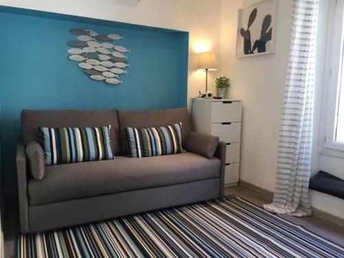 Modern studio living area at Azur Studios Cannes with gray sofa bed, striped rug, turquoise accent wall and fish wall art
