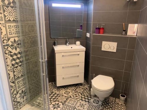 Modern bathroom at Azur Studios Cannes with white vanity, toilet, decorative floor tiles, and illuminated mirror
