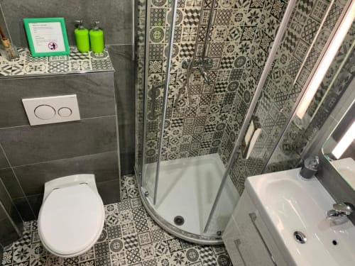 Modern bathroom with geometric patterned tiles, shower enclosure, toilet, sink, and green toiletries at Azur Studios Cannes