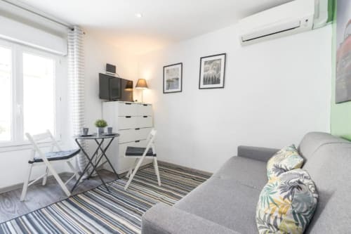 Modern studio apartment at Azur Studios Cannes with gray sofa, work desk, white dresser, and city view from window