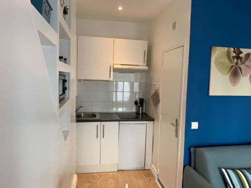 Modern kitchenette in Azur Studios Cannes Superior Studio with white cabinets, black countertop, and bright blue accent wall