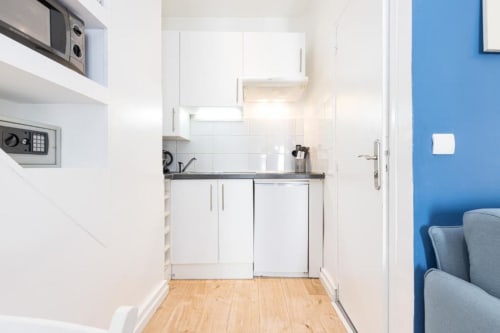 Modern kitchenette in Superior Studio at Azur Studios Cannes with white cabinets, dark countertop, hardwood floors, and blue