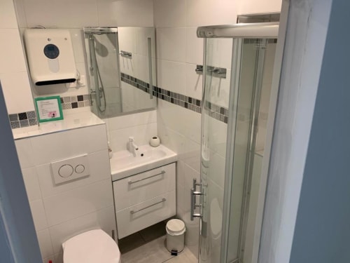Modern bathroom in Azur Studios Cannes with white tiles, glass shower enclosure, vanity sink, toilet, and decorative tile