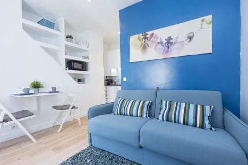 Modern studio apartment at Azur Studios Cannes featuring blue accent wall, sofa bed, kitchenette, and workspace