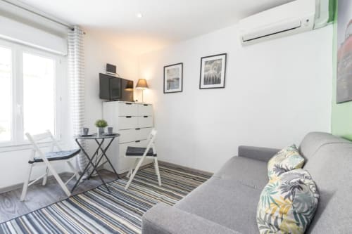 Modern studio apartment at Azur Studios Cannes with gray sofa, work desk, white dresser, and striped rug