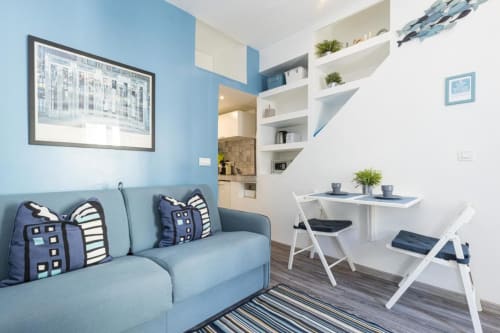Modern studio apartment at Azur Studios Cannes with blue sofa, white shelving, desk workspace, and kitchen area