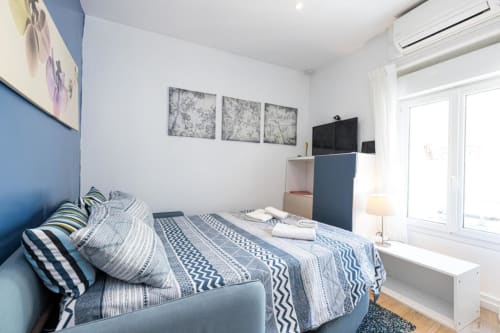 Modern bedroom at Azur Studios Cannes with blue headboard, striped bedding, TV, and bright natural light from balcony doors