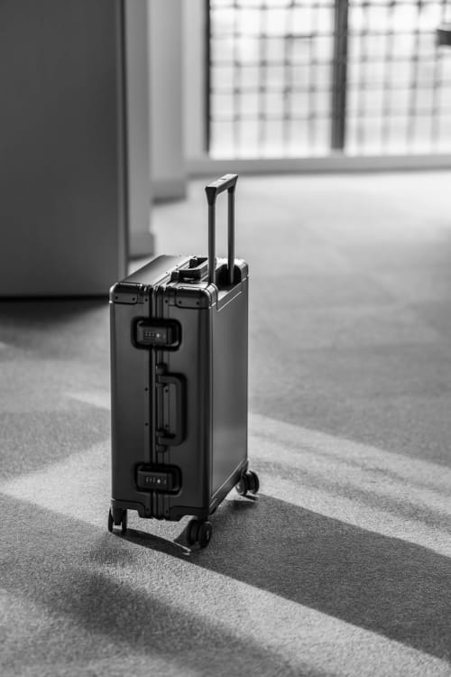 Black hardcase luggage with retractable handle on carpeted floor at Azur Studios Cannes hotel corridor