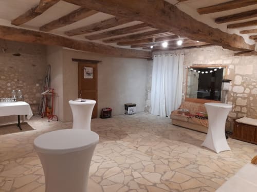 Espace événementiel rustique au Château de Ré avec poutres en bois apparent, tables de cocktail blanches et carrelage neutre au Petit