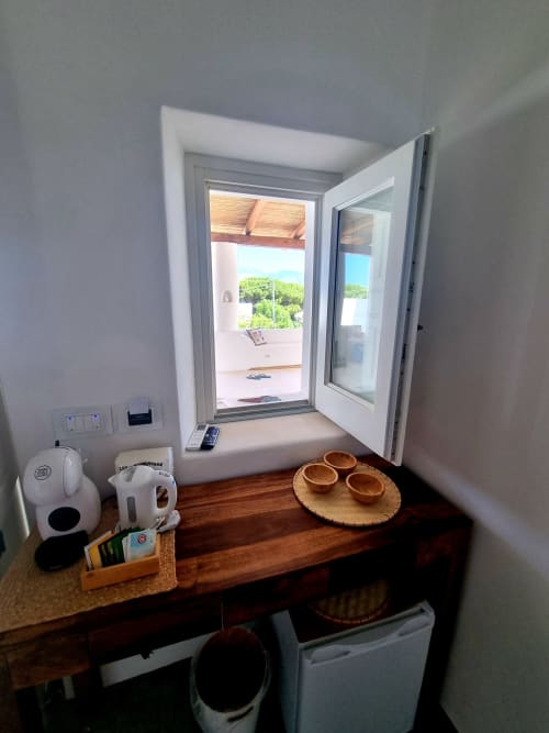 Zimmer-Fenster im Miravilla Salina B&B mit Meerblick, Kaffeemaschine, Holzschreibtisch und Terrasse mit Blick auf die Insel Salina