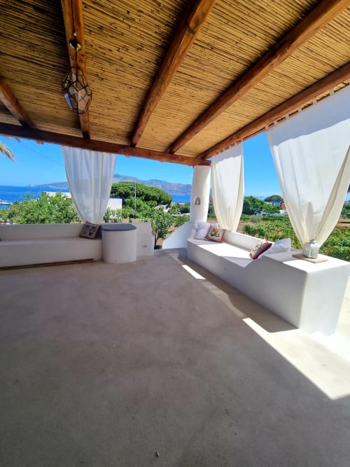 Miravilla Salina Terrasse mit Meerblick, weißen Liegestühlen, hölzerner Pergola und transparenten Vorhängen mit Blick auf die Insel Salina