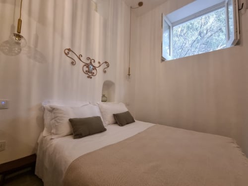 Modernes Schlafzimmer in der Miravilla Salina B&B auf Salina mit weißem Bettzeug, dunklen Kissen, Wanddekoration und Meerfenster
