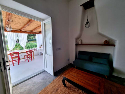 Modernes Zimmer im Miravilla Salina mit Meerblick, grünem Sofa, Holzregal und Zugang zur Terrasse mit roten Stühlen