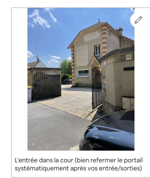 Entrée de la cour de la Suite d'amour B&B à Chartrettes avec portail noir, dallage en pierre et bâtiment couleur crème