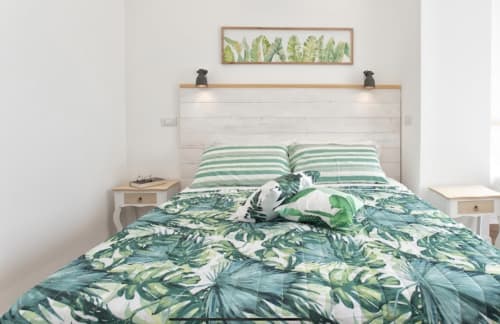 Modern bedroom at Catalogna10 with tropical leaf bedding, white shiplap headboard, and green striped pillows in Alghero