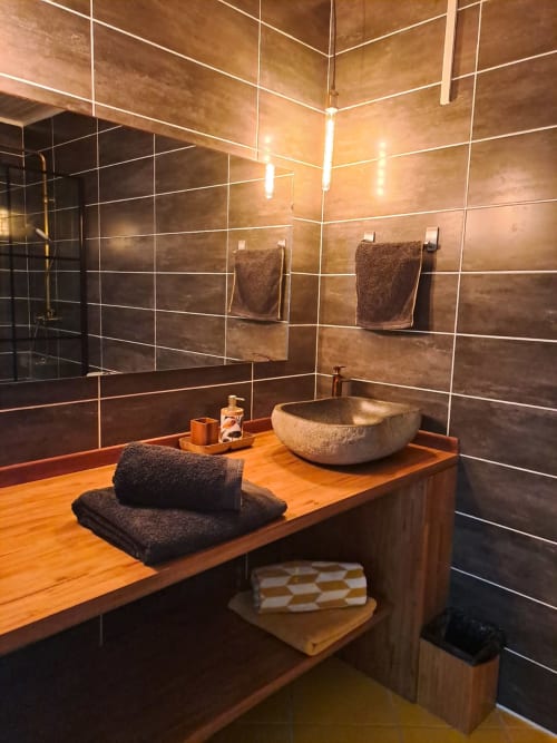 Salle de bains luxueuse à la Villa Tourmaline avec vasque en pierre, murs en carrelage marron, meuble-lavabo en bois et serviettes foncées au Lorrain