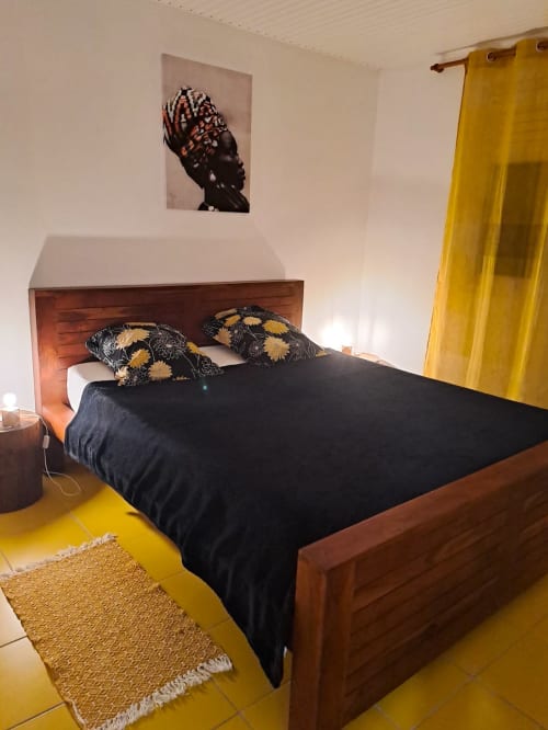 Chambre moderne de la Villa Tourmaline avec lit en bois, literie noire, accents jaunes et art africain au Lorrain, Martinique