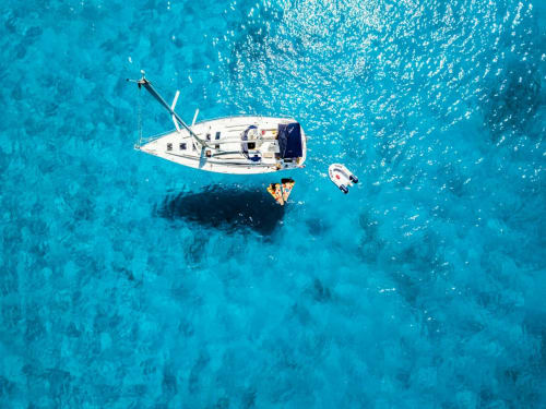 Vista aérea de velero blanco fondeado en aguas turquesas frente a Bungalow Buda Beach, Chipiona España